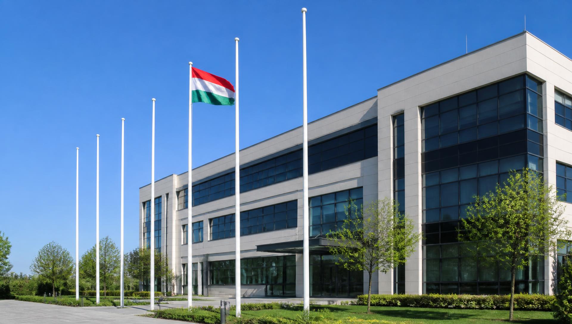 Fehér alumínium zászlórudak sora egy modern irodaépület előtt, magyar zászlóval